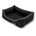 Napzzz divan hondenmand in zwart in zijaanzicht. Mand is zeer stevig gevuld in de opstaande randen en voorzien van een uitneembaar ligkussen met schuimrubber matras als vulling. Mand en ligkussen zijn beide voorzien van ritssluiting. De randen zijn verhoogd en voorzien van aparte binnenhoezen met schuimvlok, zodat de buitenhoes eventueel gewassen of gelucht kan worden. De stof is oxford dus waterafstotend en is mooi afgewerkt en geborduurde Napzzz logo. Luxe en comfortabel en in meerder maten verkrijgbaar.