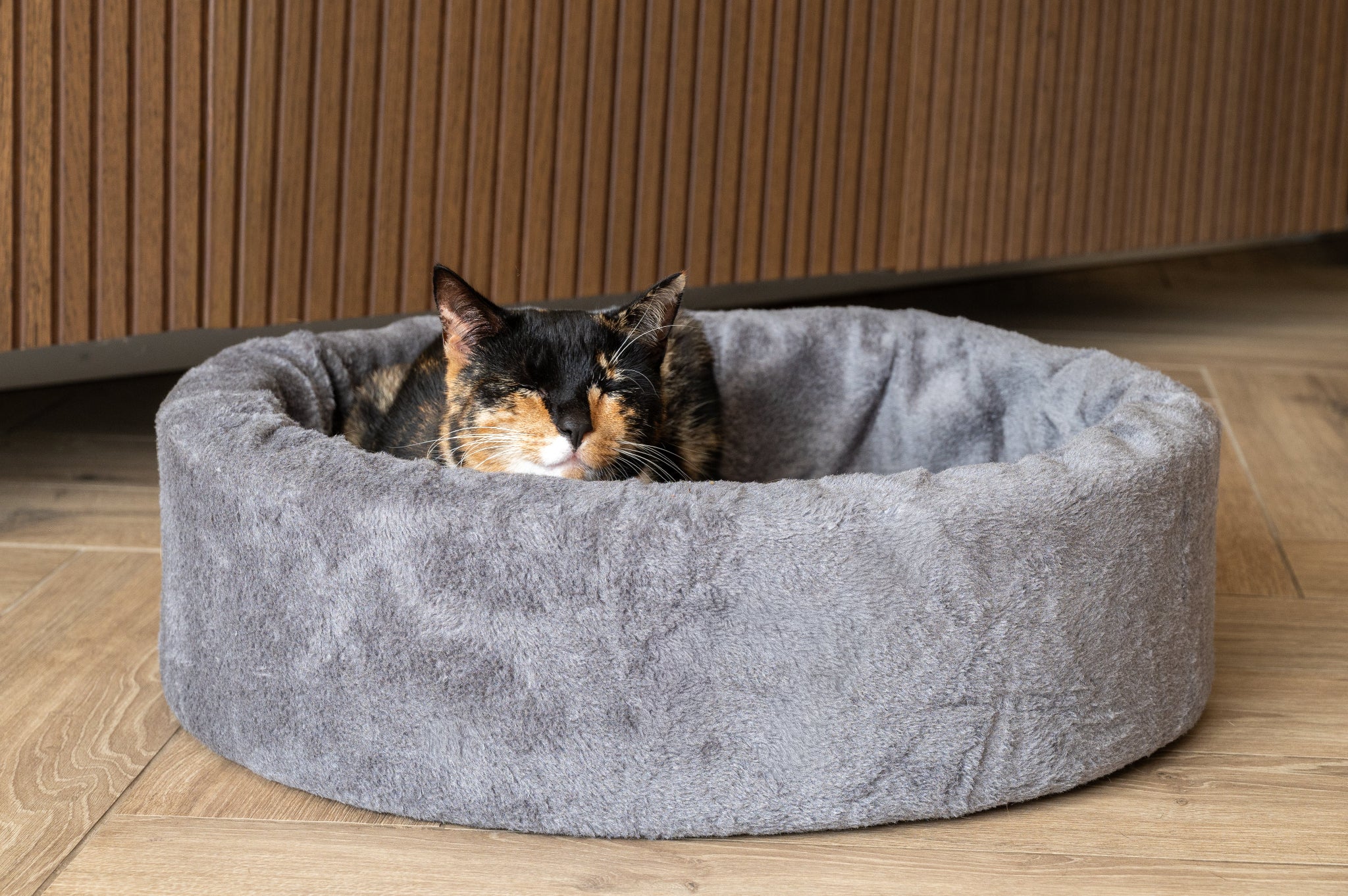 Kat liggend in een kleine ovale NapZZZ bontmand grijs, knusse en comfortabele ligplek voor katten en kleine honden