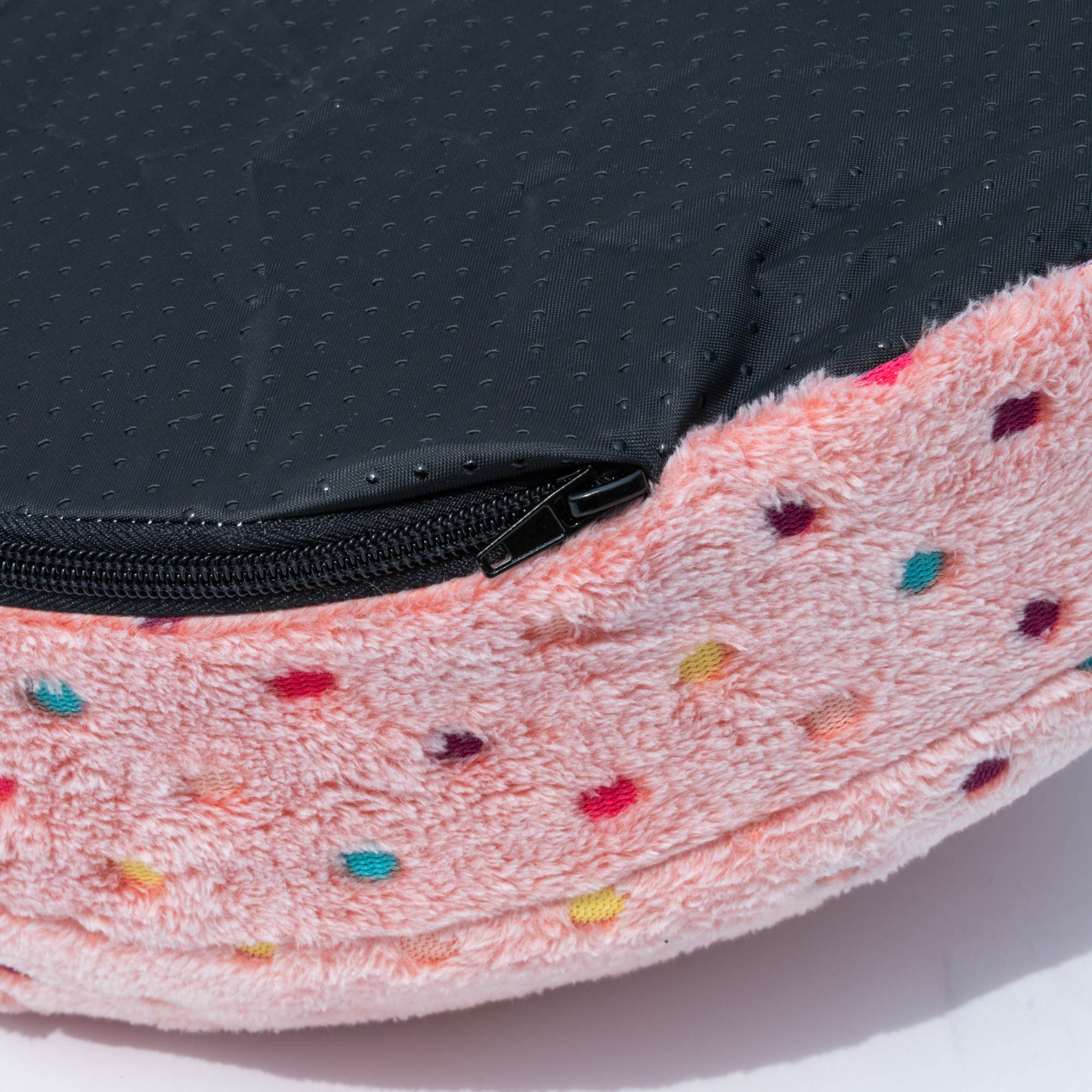 Napzzz cuddle cave dotz voor kat of kleinere hond in roze kleur in detail onderaanzicht. Antislip bodem en rits. Schuimrubber matras met zacht pluche hoes voorzien van gekleurde stippen. Opstaande bovenkant dat werkt als deken en zorgt voor knusse ligplek. 